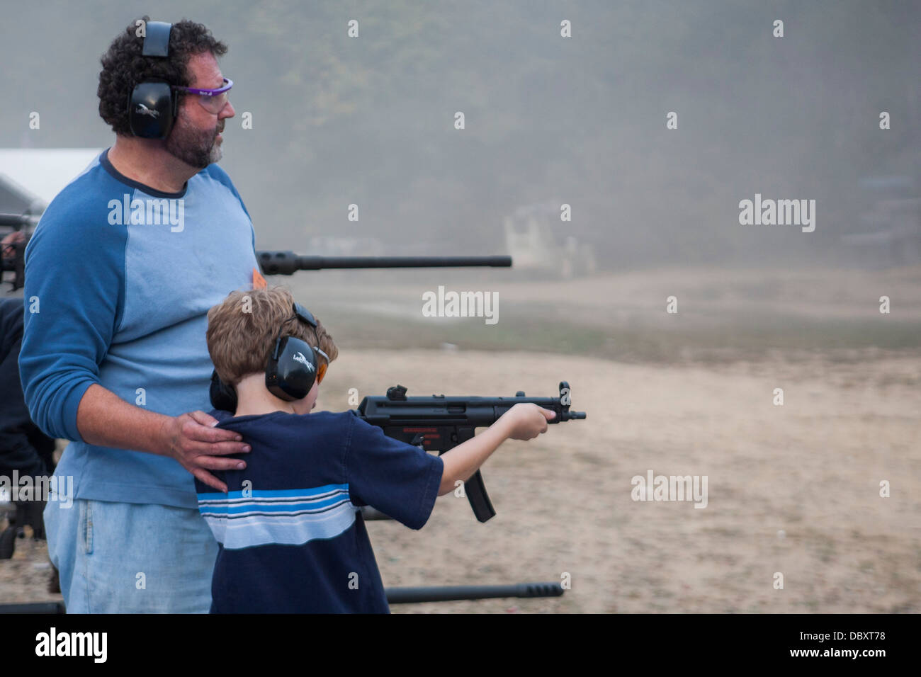 A father helping his young son fire a machine gun at the Knob Creek Machine Gun Shoot Stock