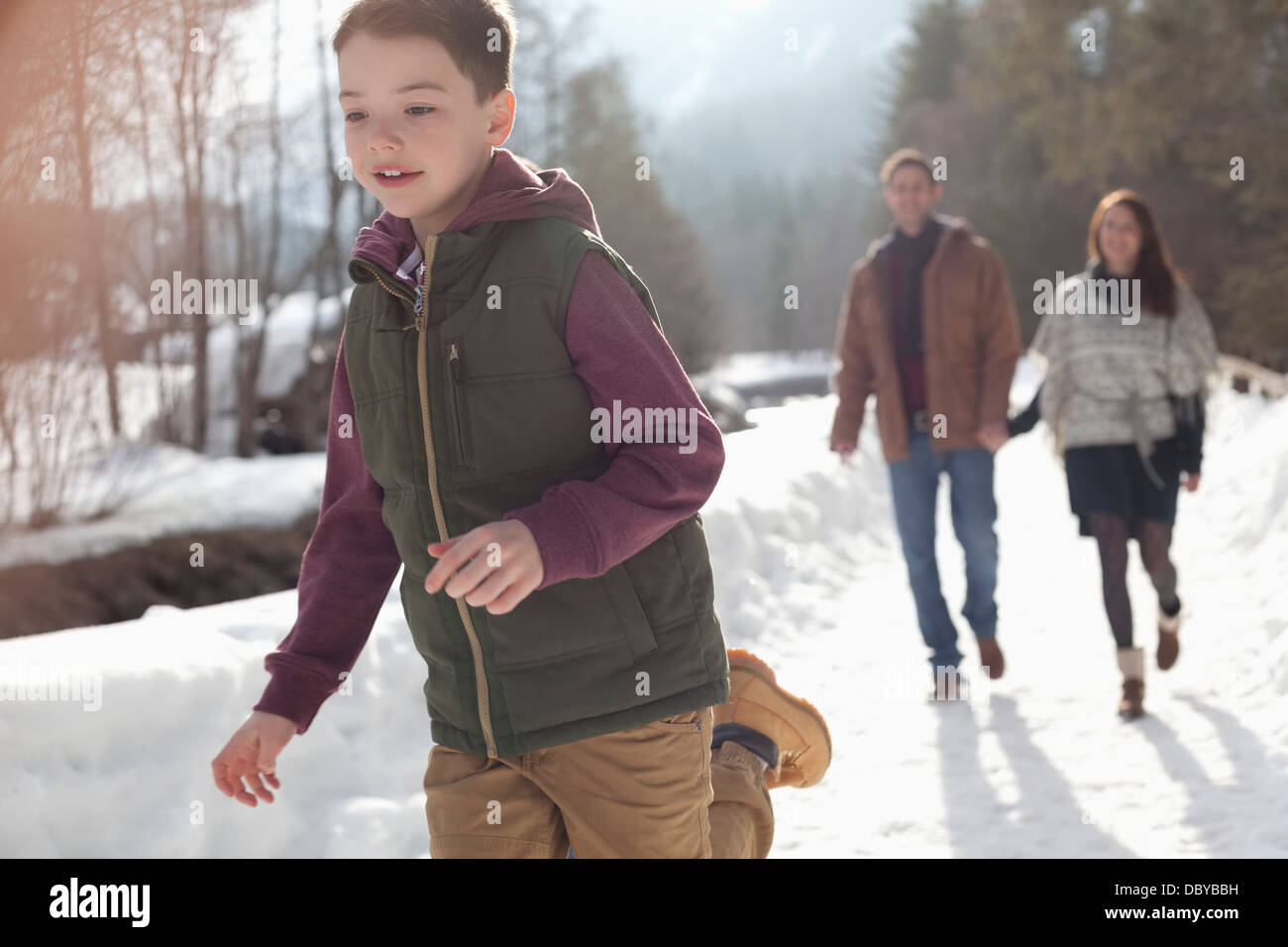 Parents watching boy run in snowy lane Stock Photo