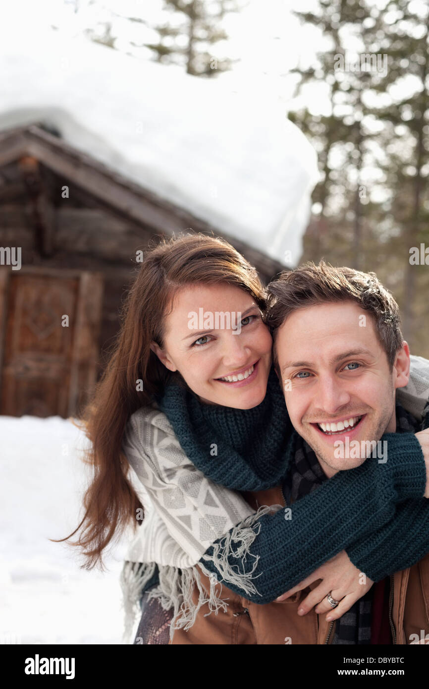 Portrait of happy couple hugging in snow outside cabin Stock Photo