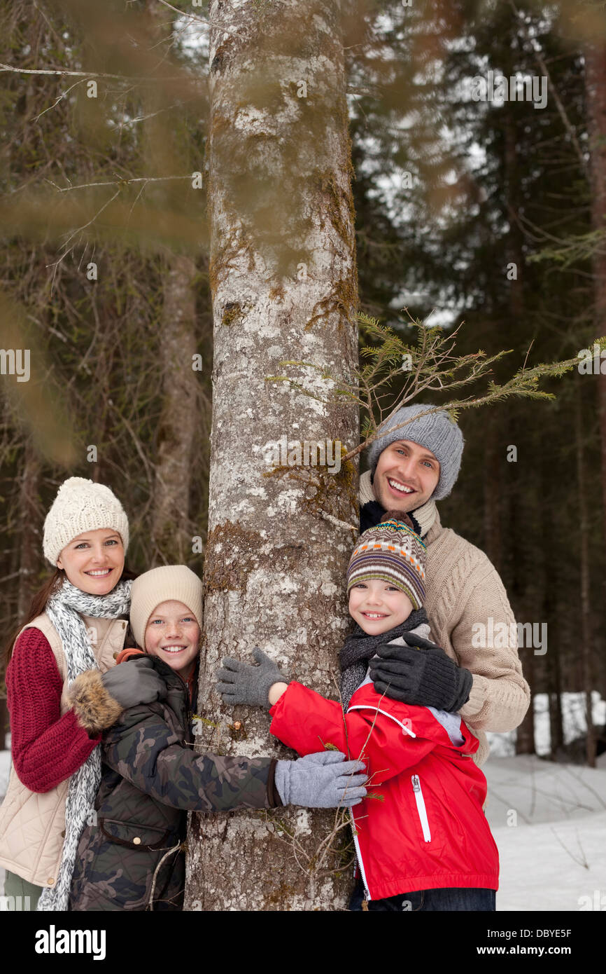 Portrait of happy family hugging tree trunk in snowy woods Stock Photo