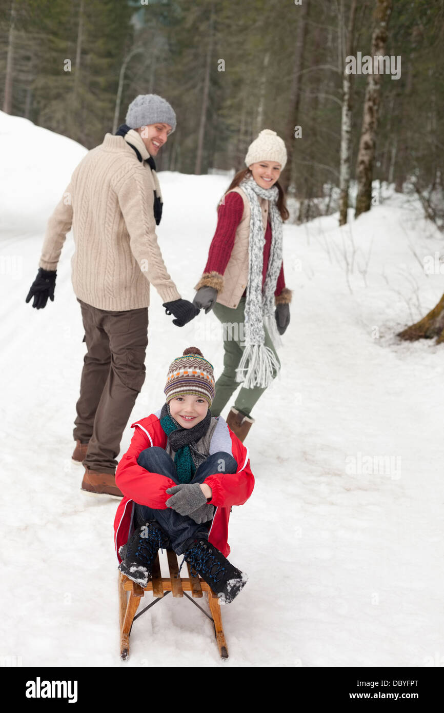 Parents pulling happy boy on sled in snowy woods Stock Photo