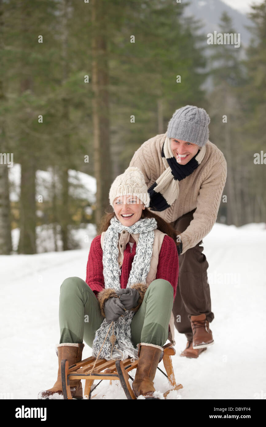 Happy couple sledding in snowy woods Stock Photo