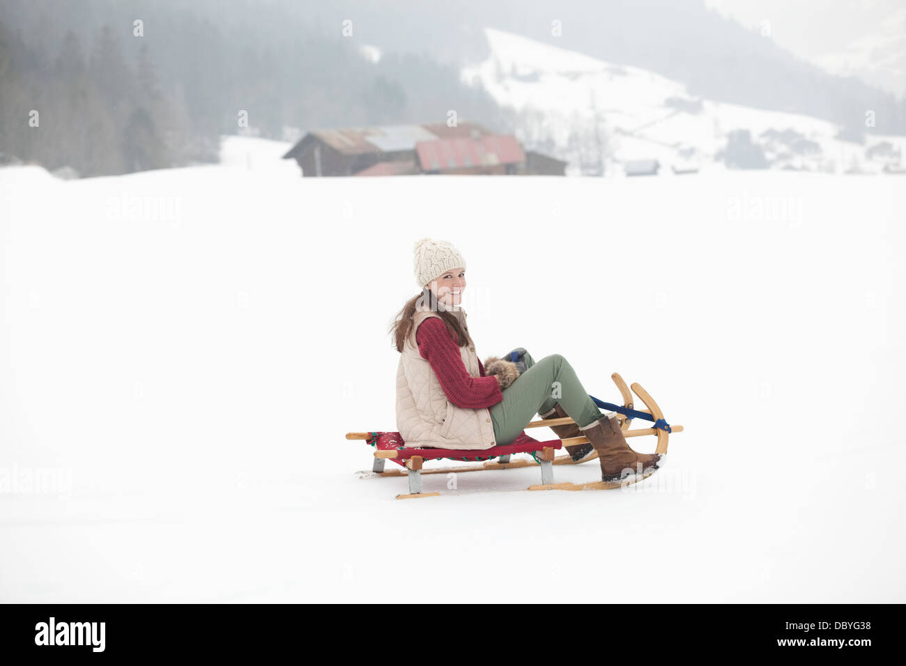 Portrait of smiling woman sledding in snowy field Stock Photo