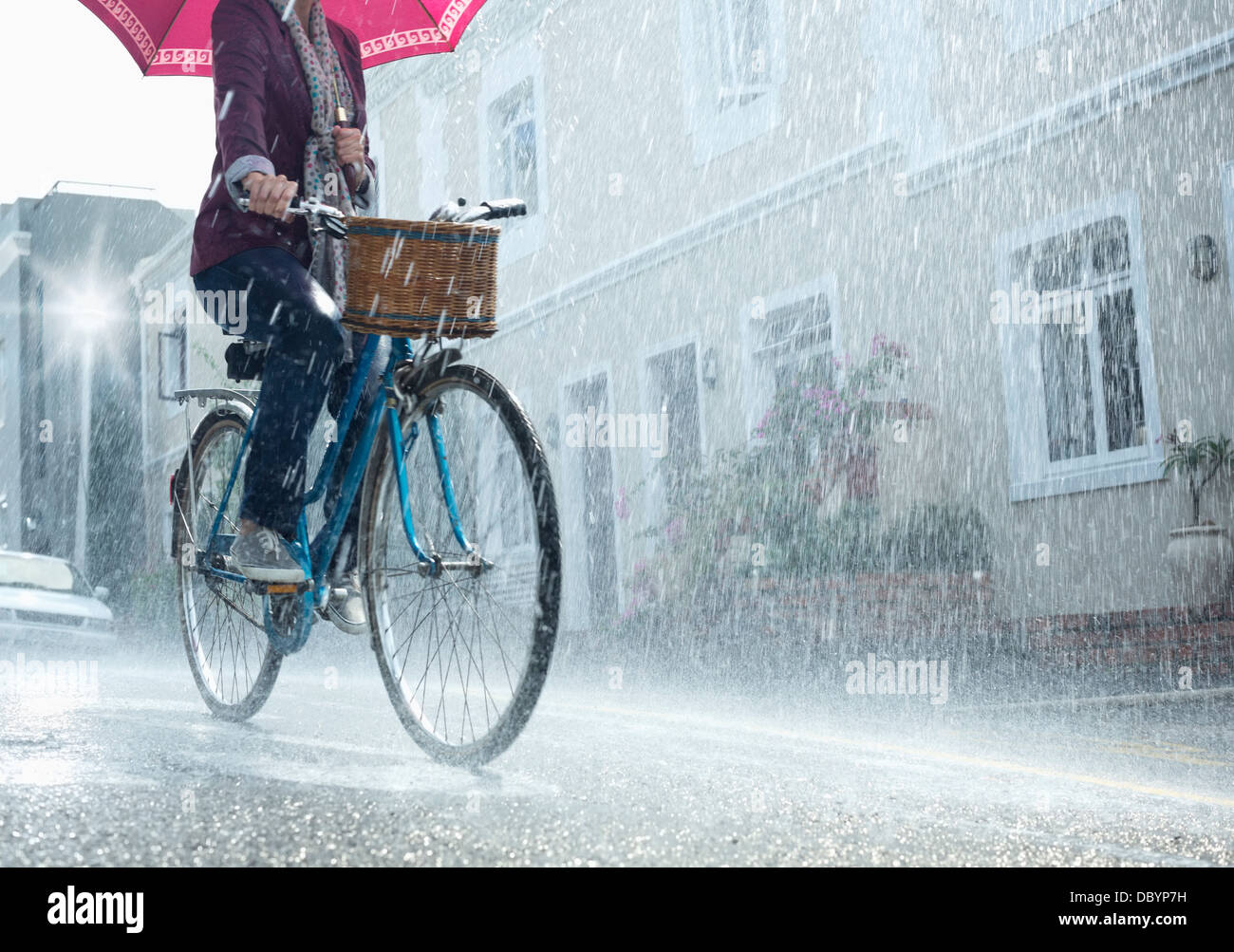 Woman riding bicycle with umbrella in rainy street Stock Photo