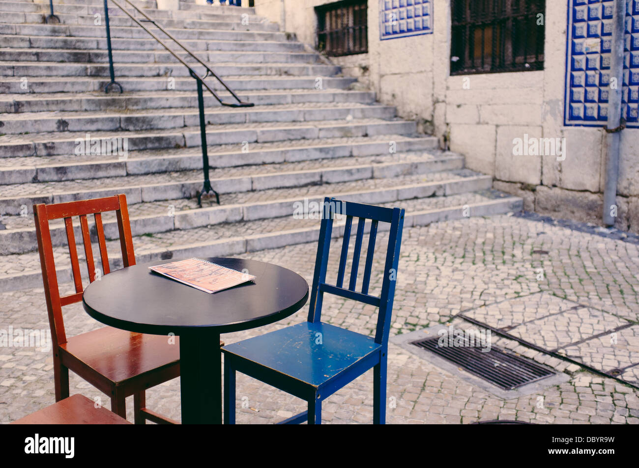 A table with two chairs waiting for customers in a street at the district of Alfama, Lisbon. Stock Photo