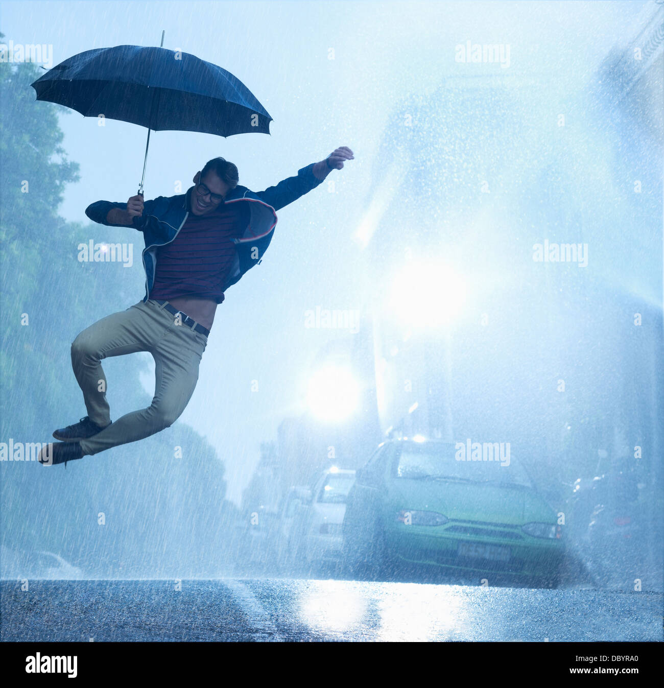 Enthusiastic man with umbrella jumping in rain Stock Photo