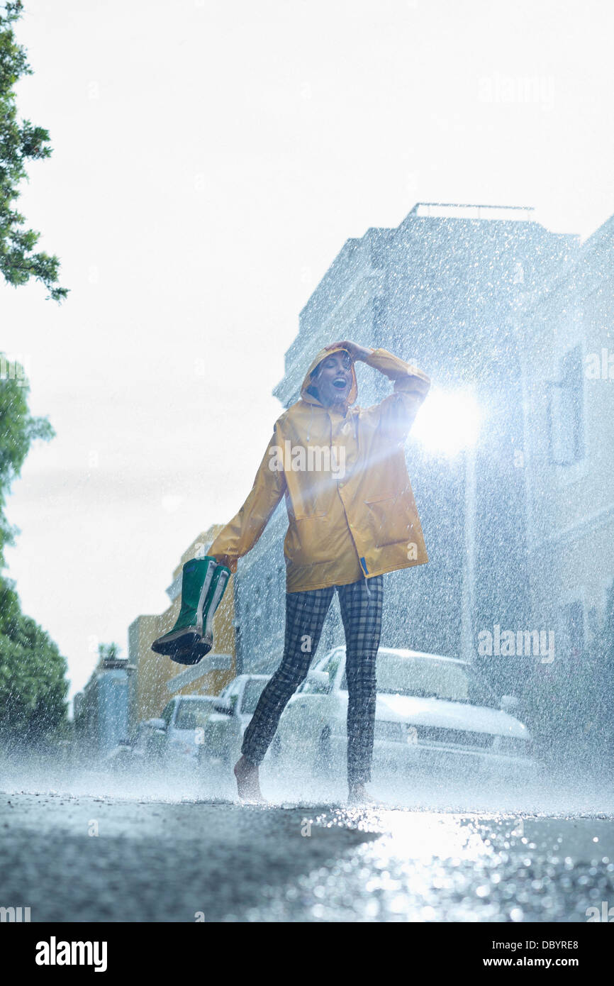 Woman in raincoat carrying wellingtons and walking barefoot in rain Stock Photo
