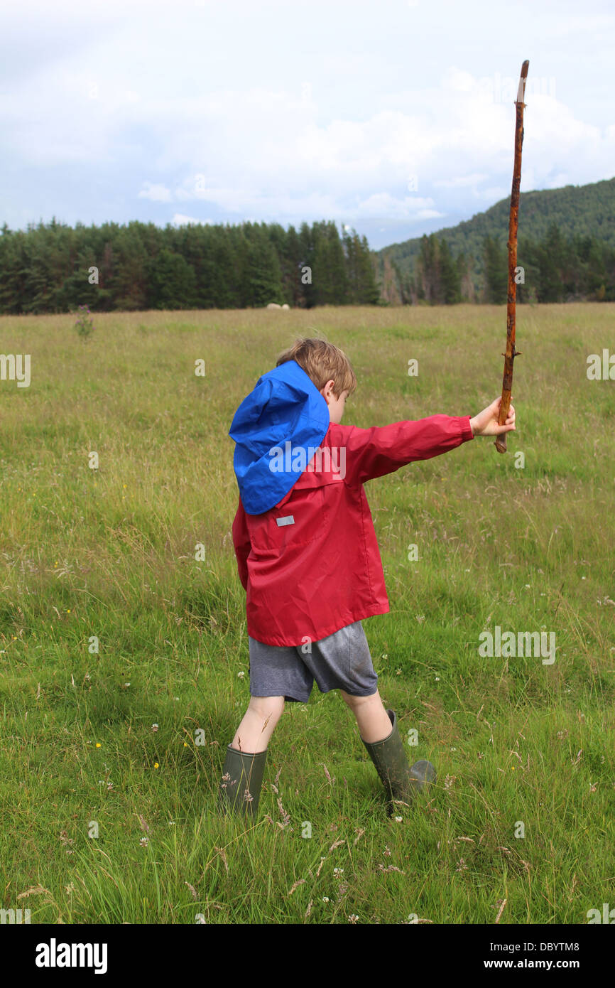 Boy walking and swinging a long stick, Scottish Highlands. Stock Photo