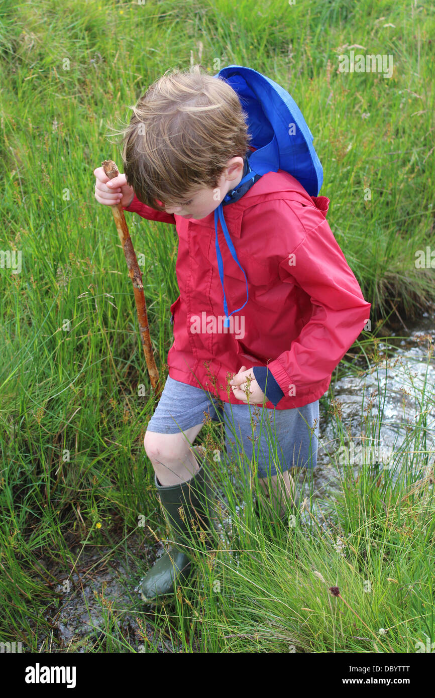 Boy paddling in a stream in wellies and anorak Stock Photo