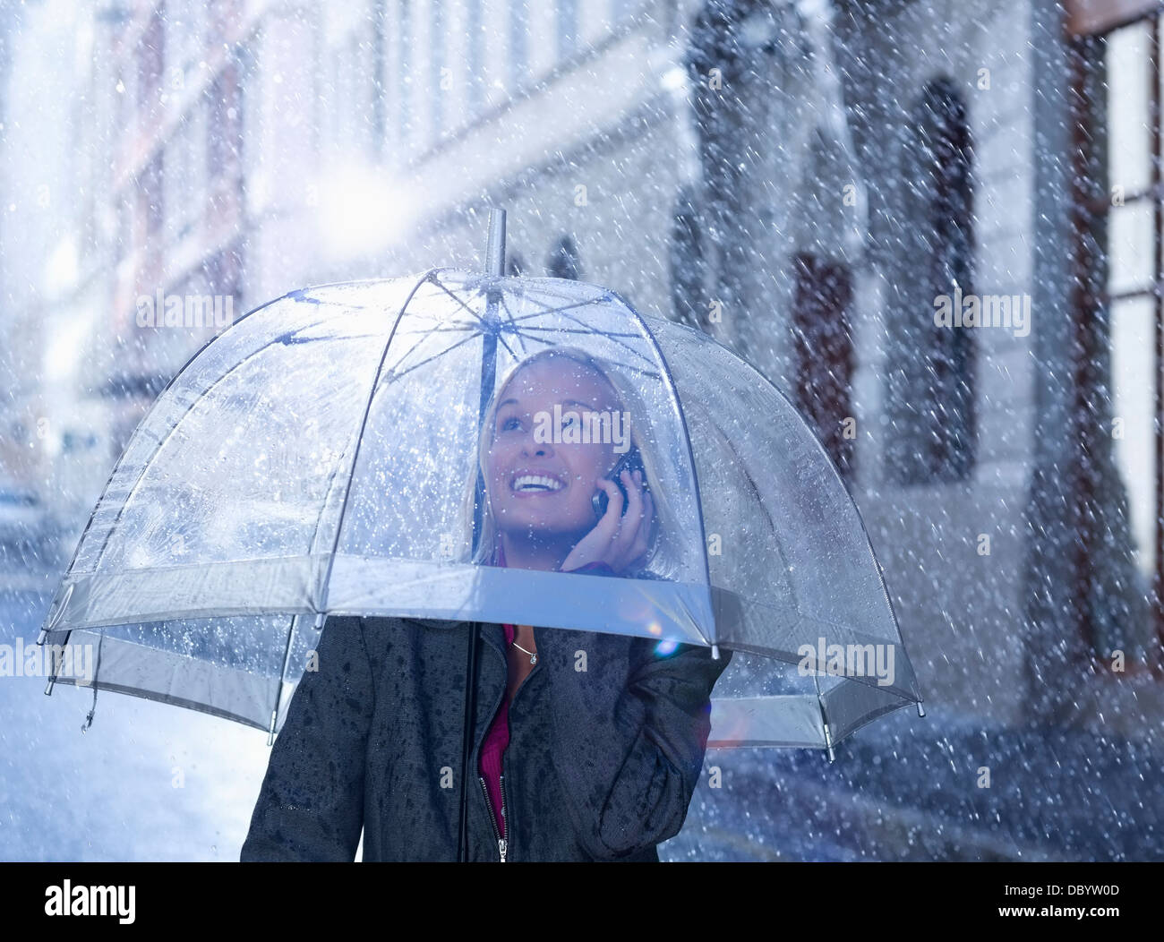 Smiling businesswoman talking on cell phone under umbrella in rainy street Stock Photo