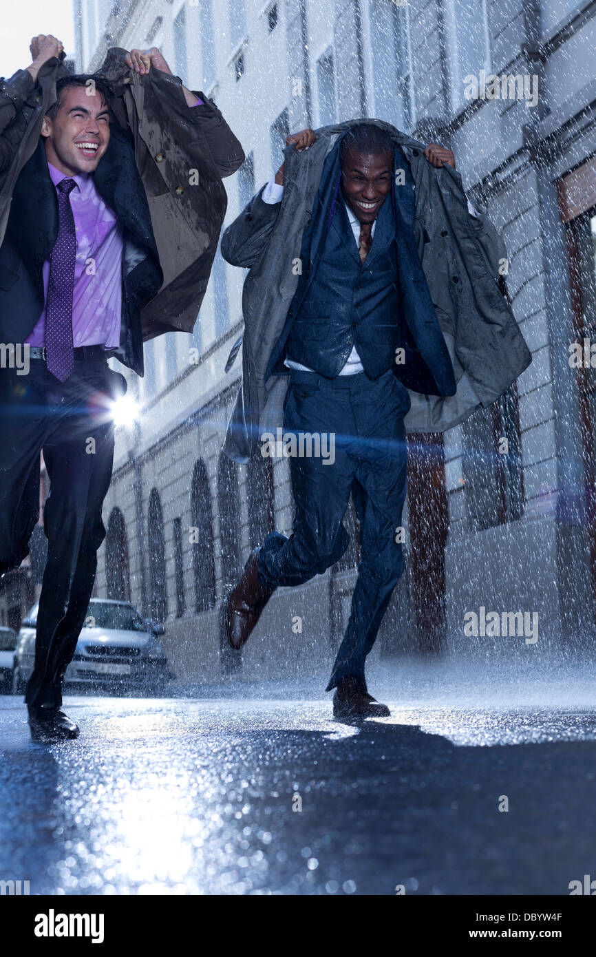 Happy businessmen covering heads with coats in rainy street Stock Photo