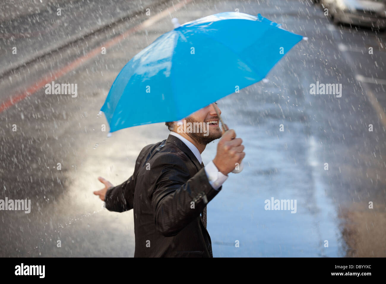 Businessman with tiny umbrella walking in rain Stock Photo