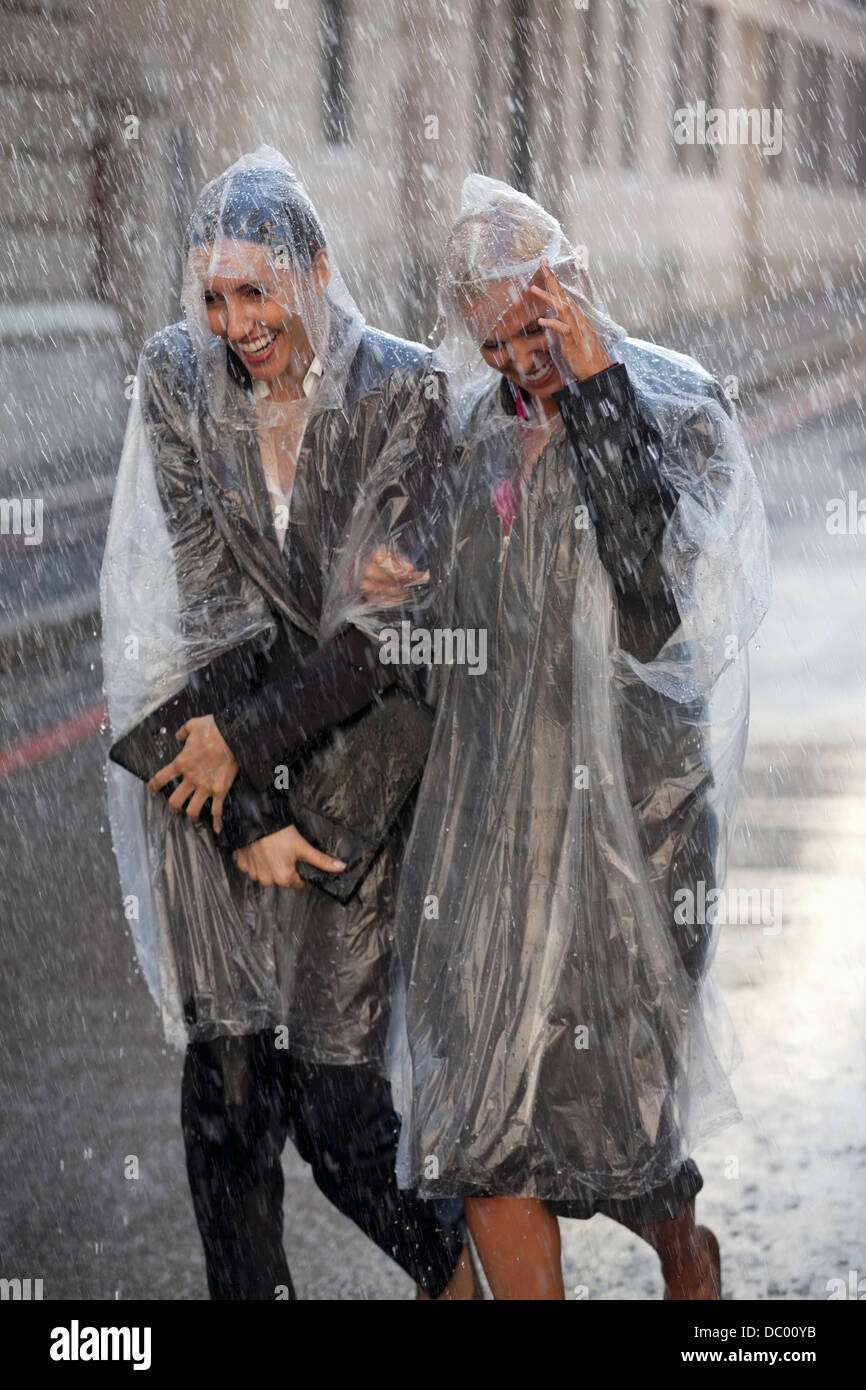 Businesswomen in ponchos walking in rainy street Stock Photo