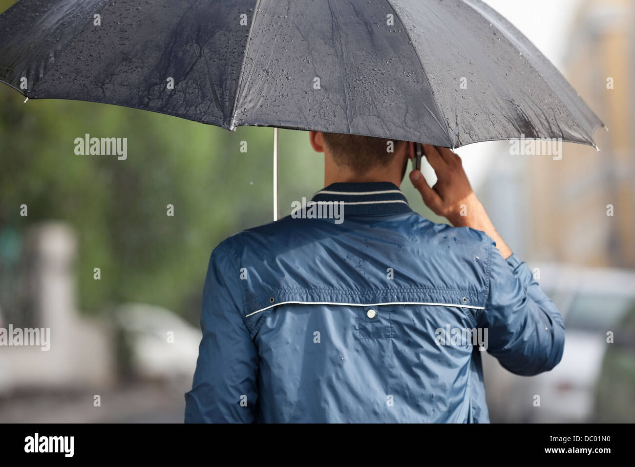 Man talking on cell phone under umbrella in rain Stock Photo