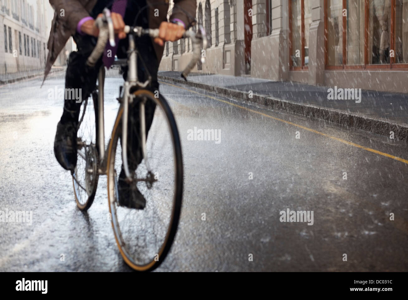 Businessman riding bicycle in rainy street Stock Photo