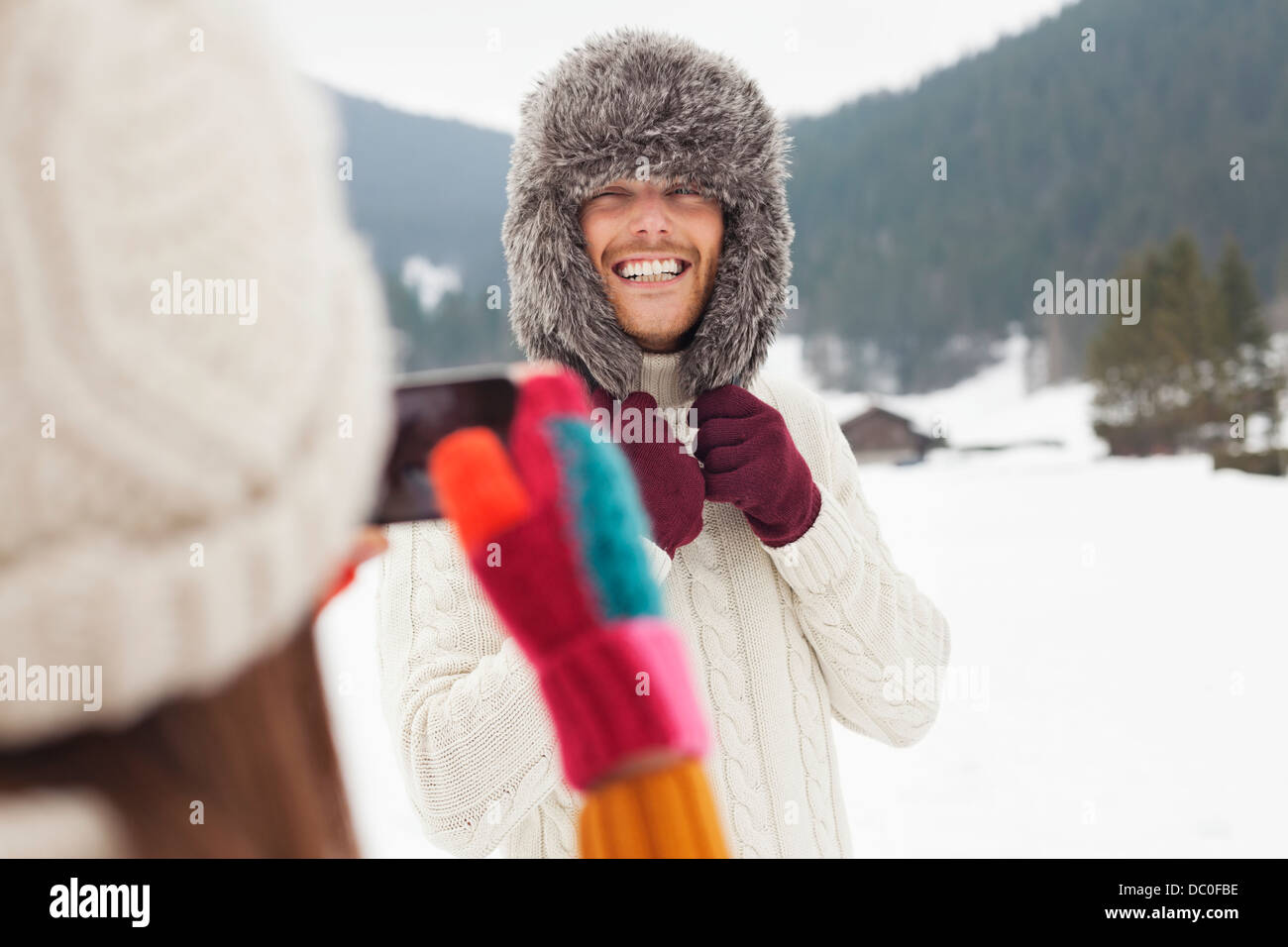 Woman photographing man wearing fur hat in snowy field Stock Photo