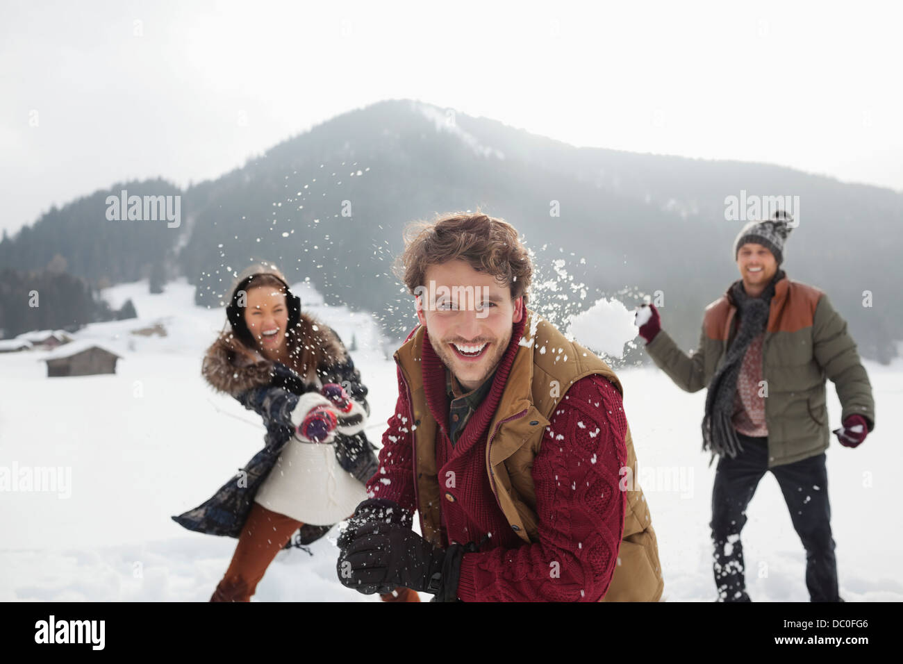 Portrait of playful friends throwing snowballs in field Stock Photo