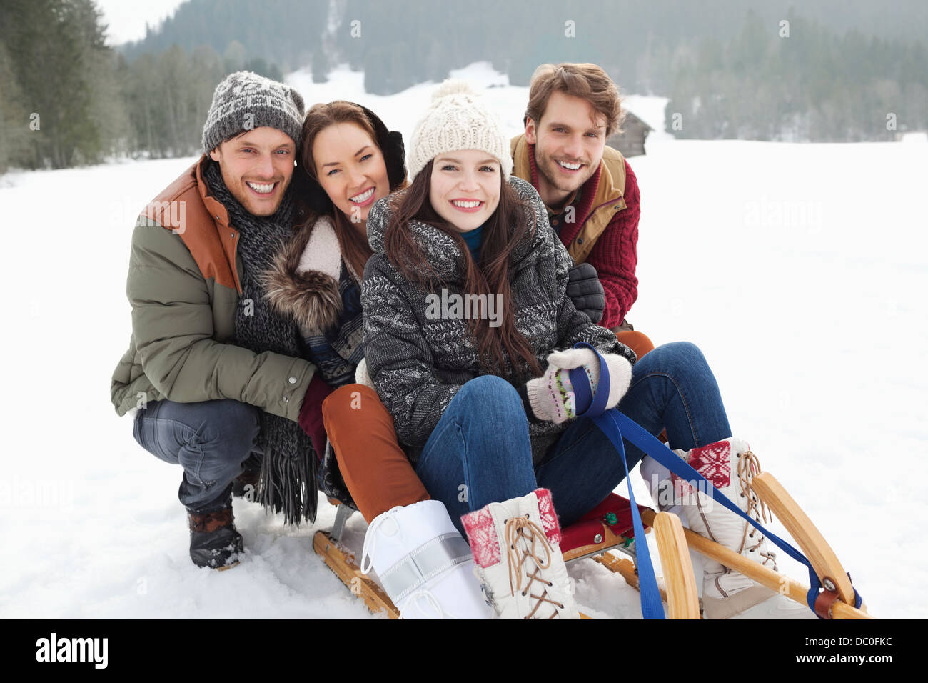 Portrait of happy friends on sled in snowy field Stock Photo