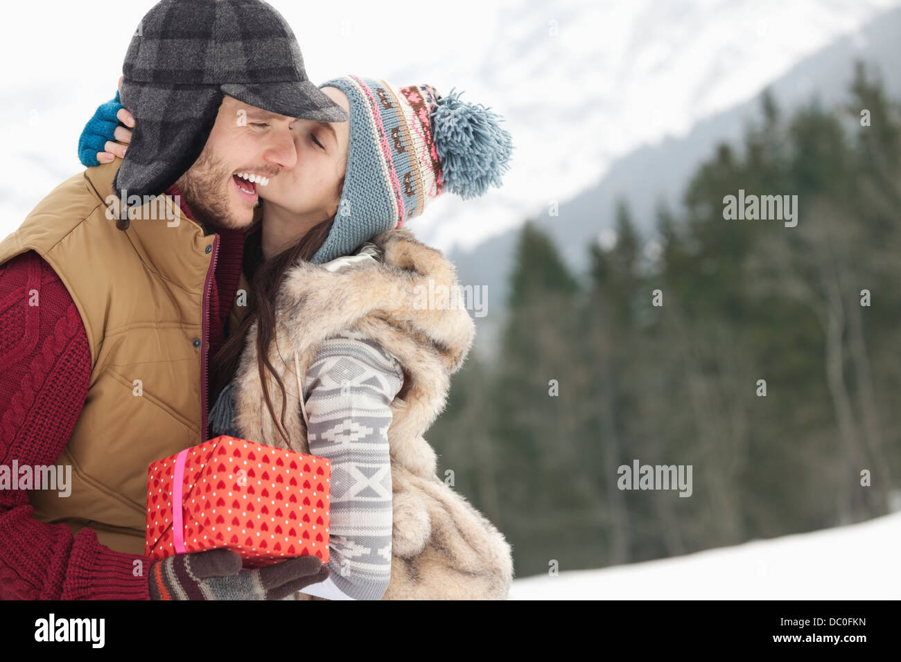Happy couple with Christmas gift kissing in snowy field Stock Photo