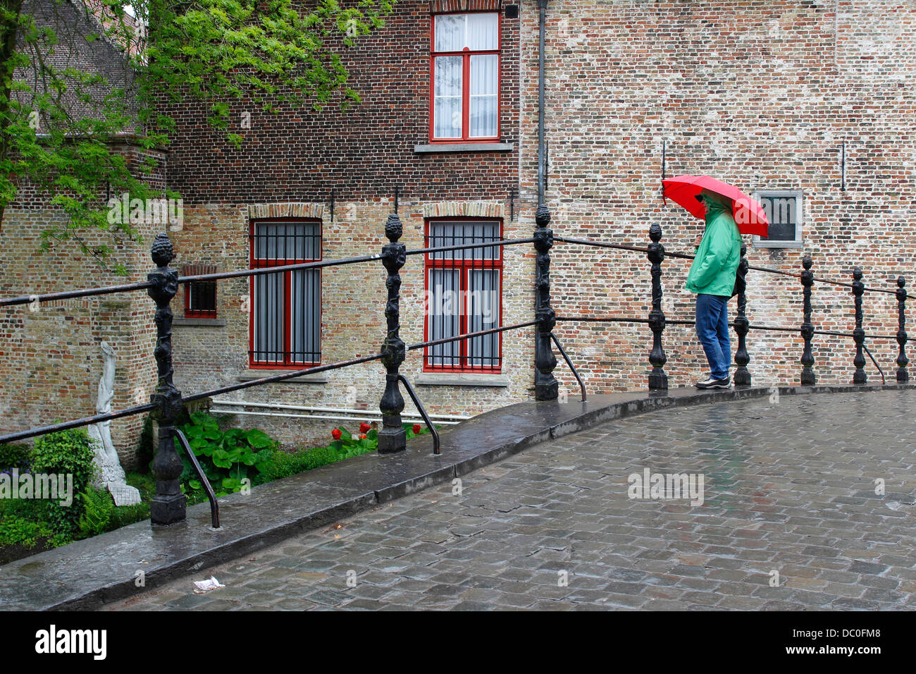 Bruges Belgium Flanders Europe Brugge woman with red umbrella in rain on bridge by Begijnhof nunnery Stock Photo