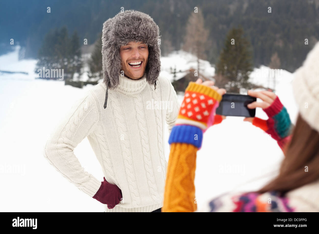 Woman photographing man in fur hat in snowy field Stock Photo