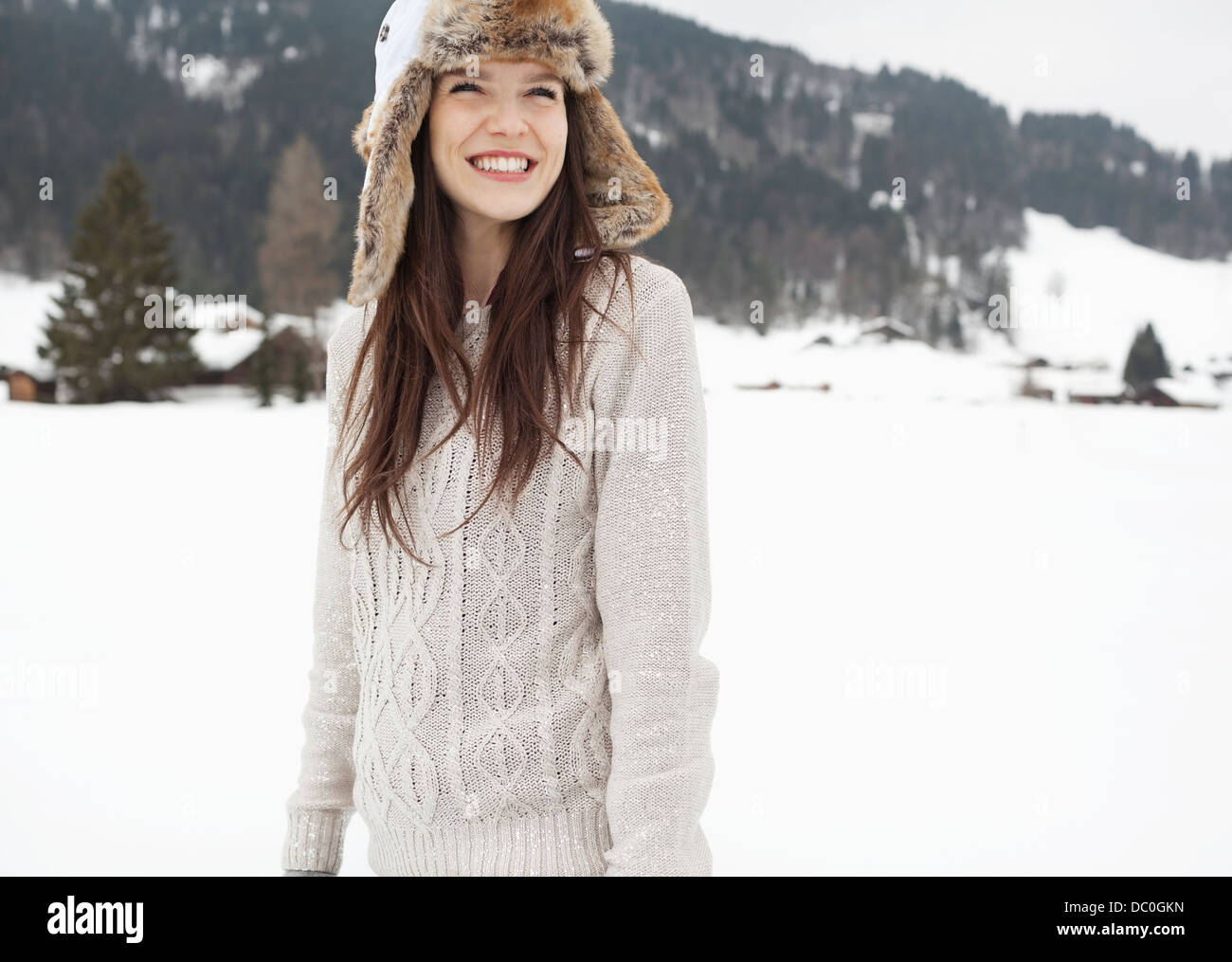 Happy woman wearing fur hat in snowy field Stock Photo