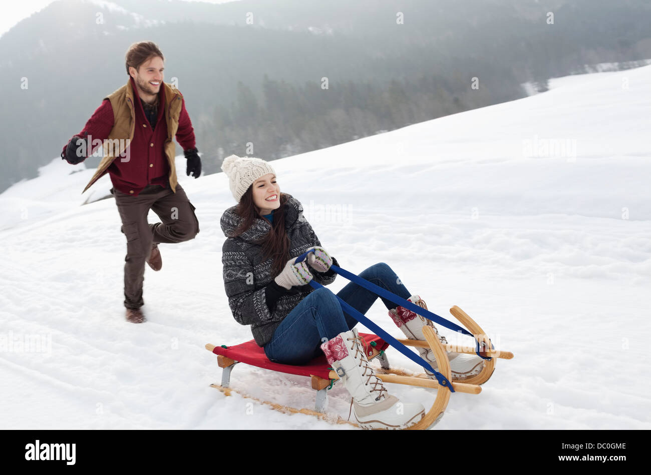 Happy couple sledding in snowy field Stock Photo
