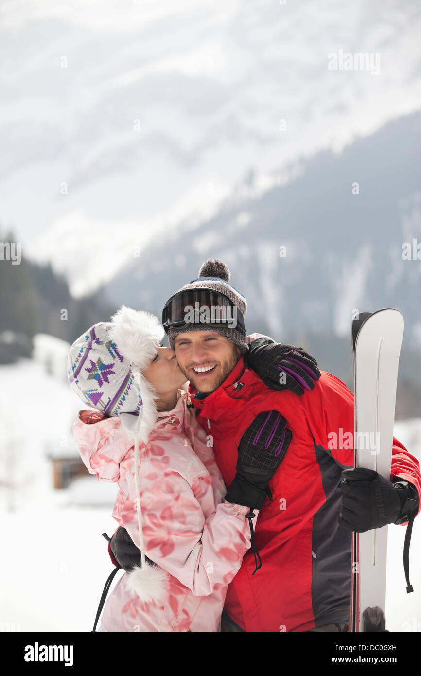 Happy couple with skis kissing in snowy field Stock Photo