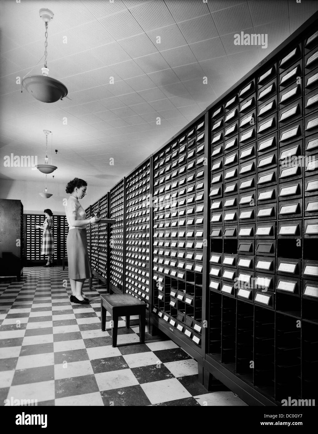 1950s 1960s TWO YOUNG WOMEN STANDING BESIDE OPEN DRAWERS OF COMPUTER PUNCH CARD FILING CABINETS Stock Photo