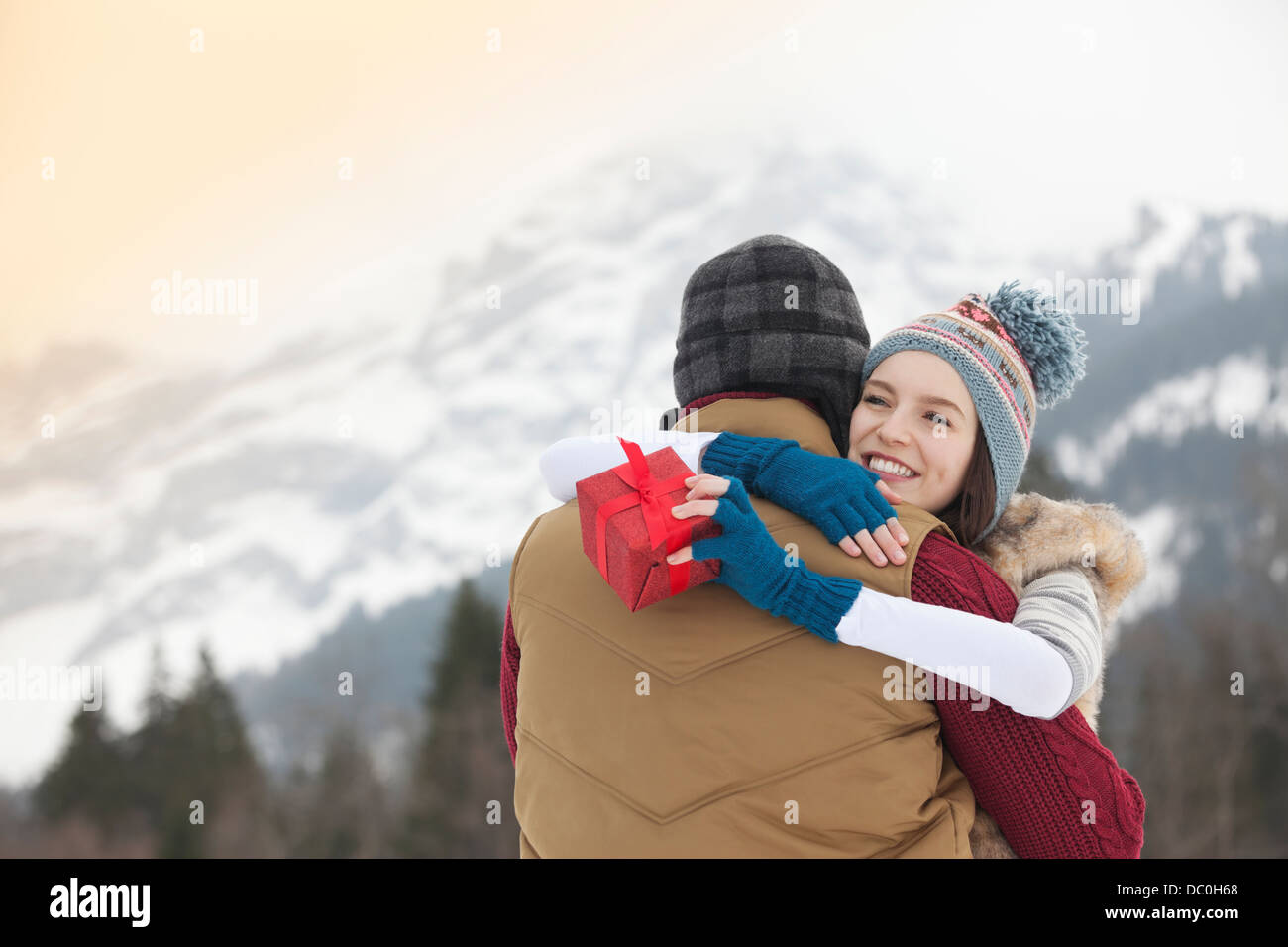 Happy woman holding gift and hugging man with mountains in background Stock Photo