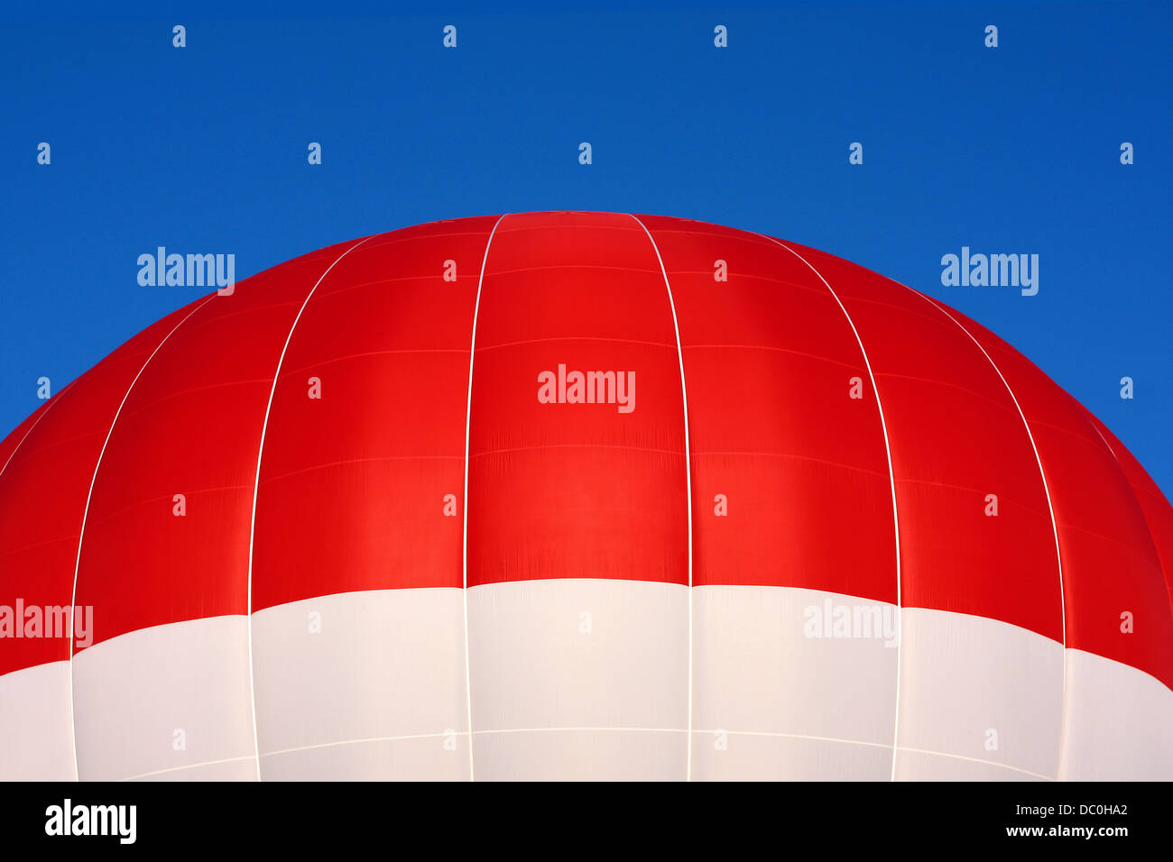 Close up of top part of a red and white hot air balloon flying in front of a brilliant blue summer sky. Stock Photo