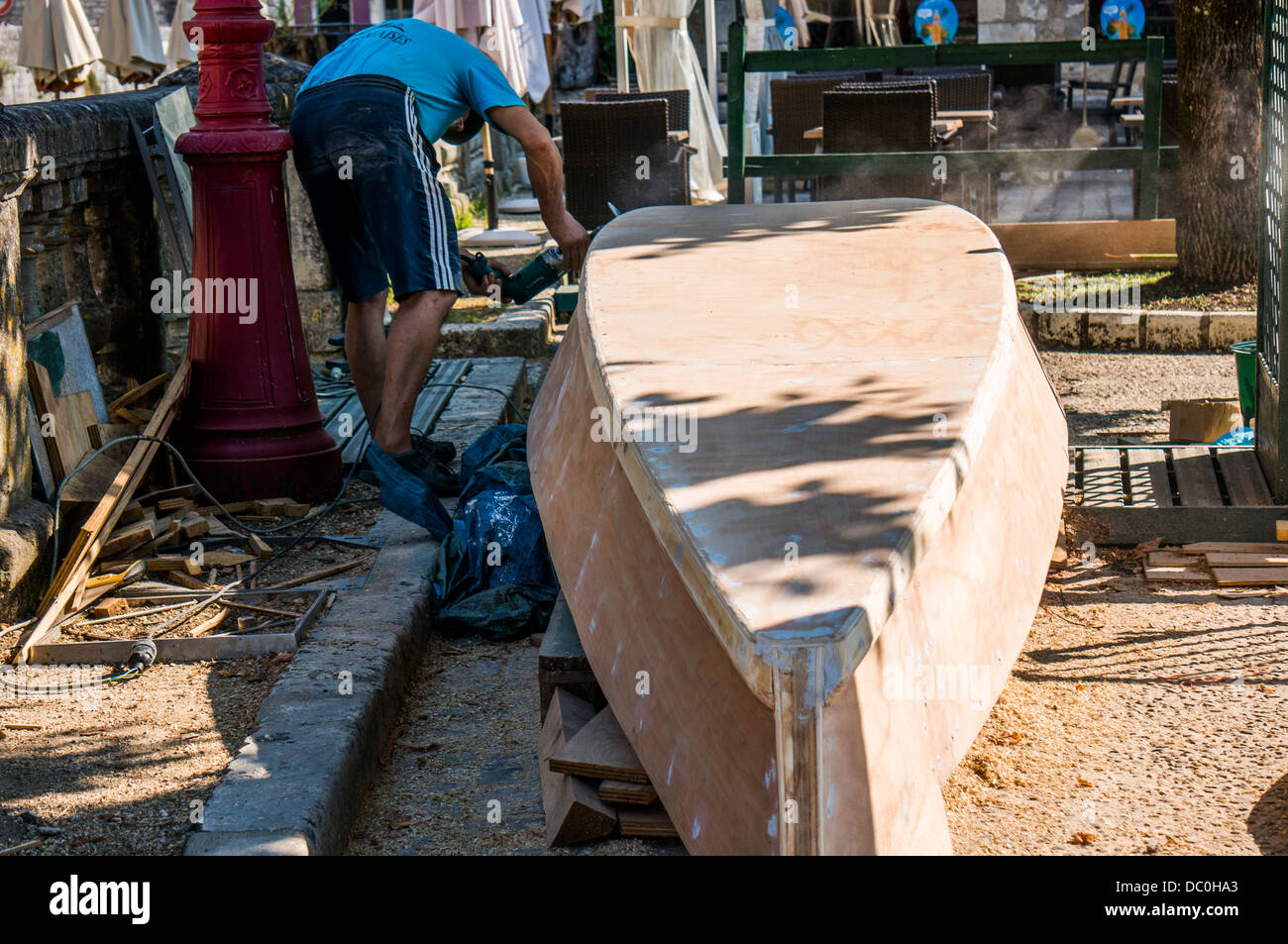 A flat bottom boat builder (for use in shallow waters), sanding the side of a boat. Brantôme, in the Dordogne department in south west France, Europe. Stock Photo