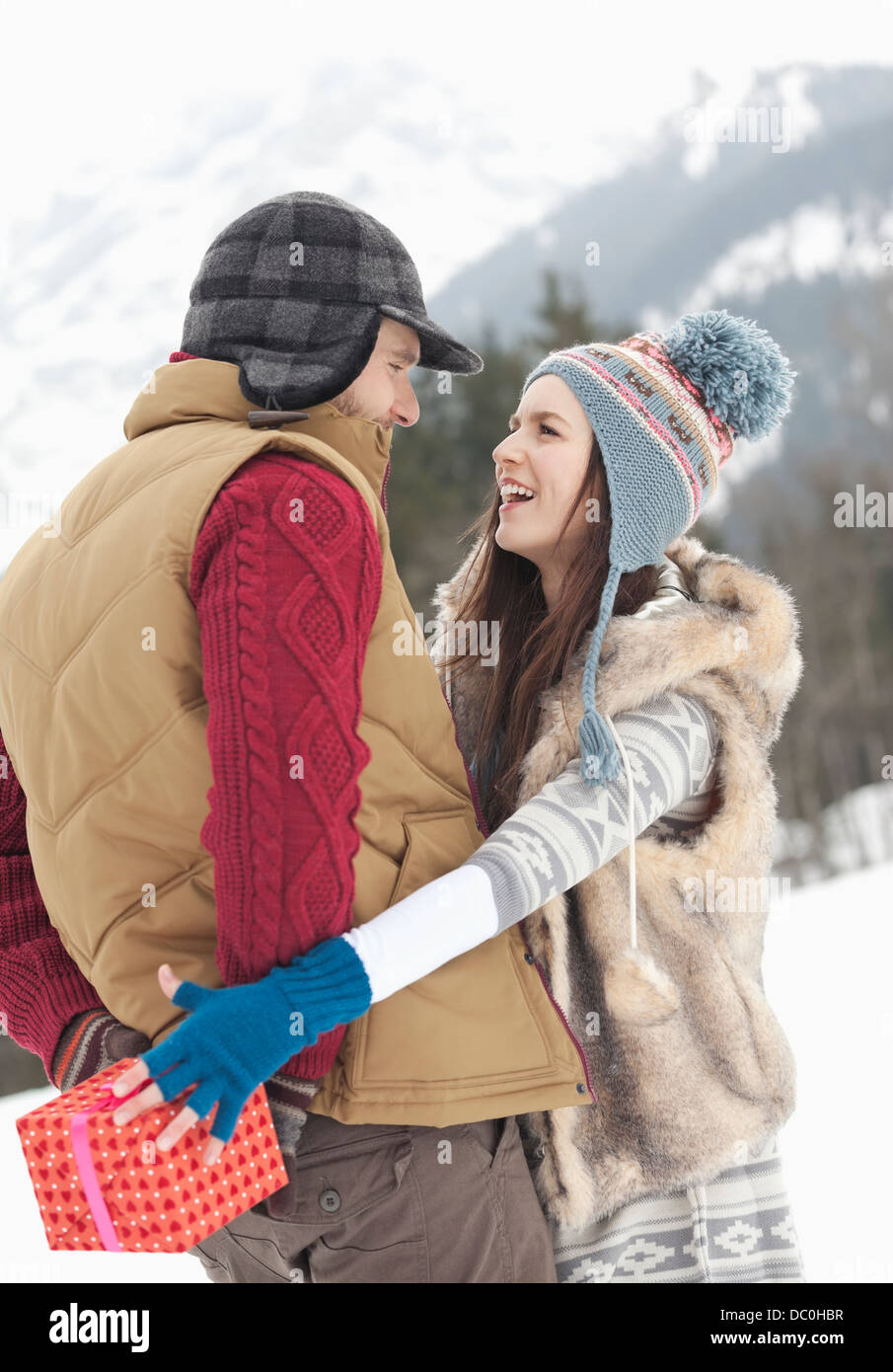 Woman reaching for Christmas gift behind man's back in snowy field Stock Photo