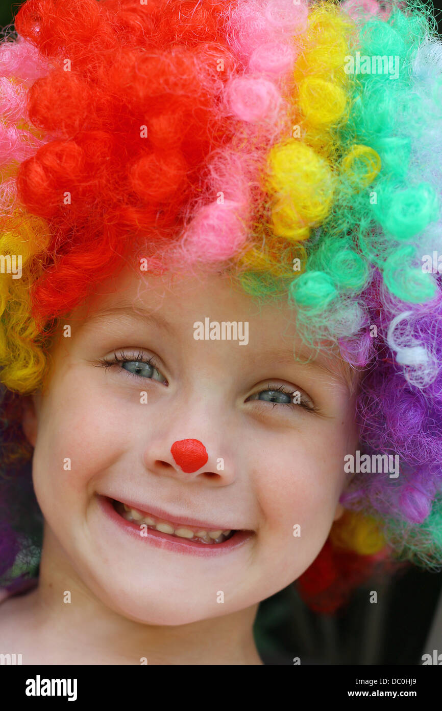 a close up of a cute, smiling toddler boy dressed up in a costume clown wig and face paint Stock Photo