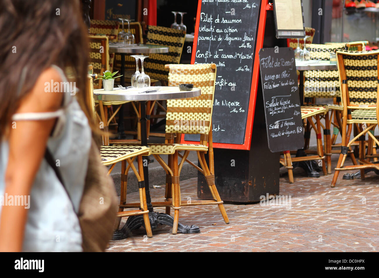 Girl passing by a cafe at rue Mouffetard - traditional wicker furniture and menu boards exposed on the pavement, Paris, France Stock Photo