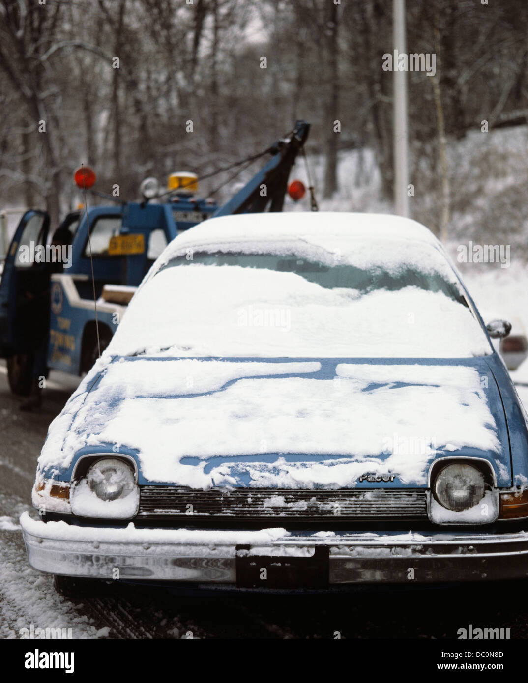 1970s CAR COVERED WITH LIGHT SNOW BEING TOWED BY TOW TRUCK Stock Photo