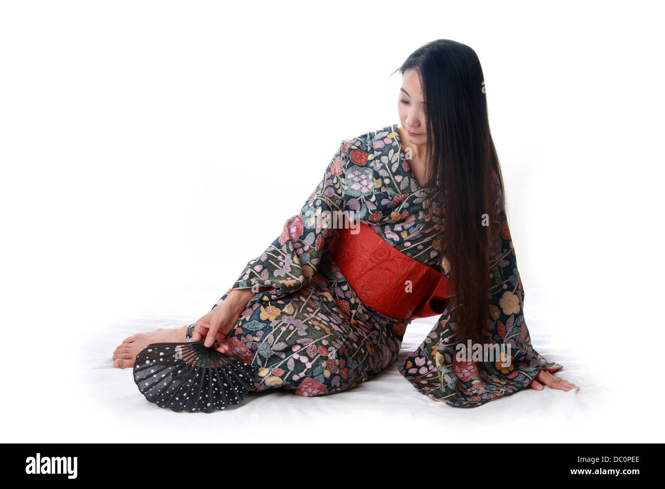 Japanese Lady Sitting on the Floor Wearing a Traditional Blue and Red Patterned Kimono and Holding a Fan Stock Photo