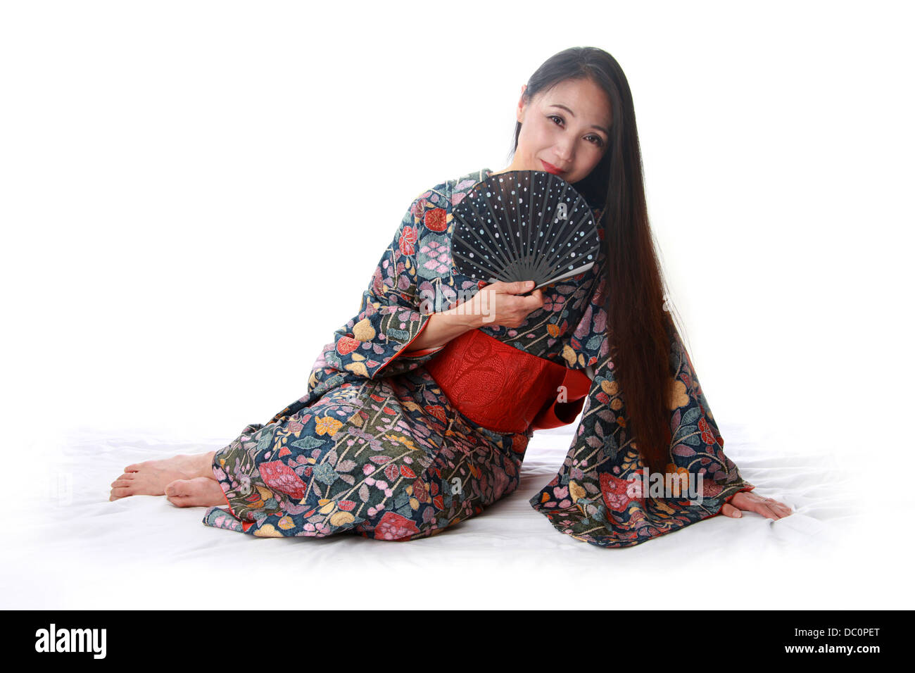Japanese Lady Sitting on the Floor Wearing a Traditional Blue and Red Patterned Kimono and Holding a Fan Stock Photo