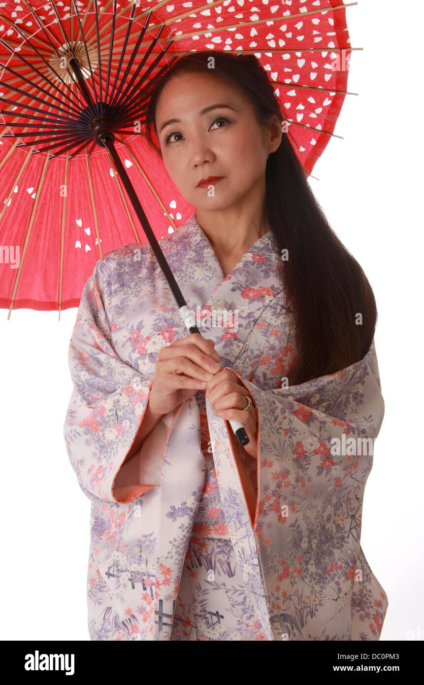 Japanese Lady Wearing a Pink and Lilac Patterned Kimono and Holding a Red Sun Shade. Stock Photo