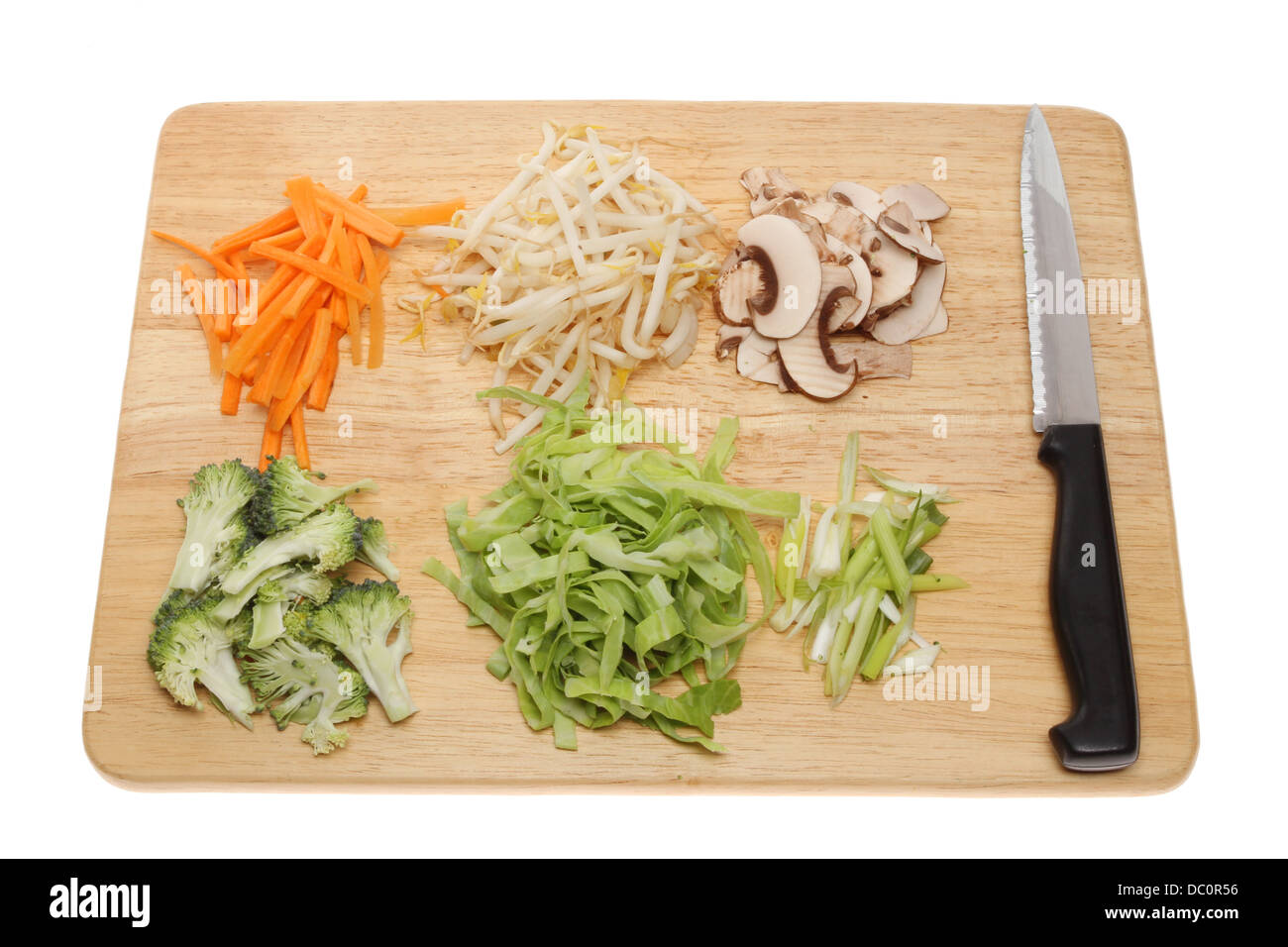 Vegetable stir fry ingredients on a wooden chopping board with a knife isolated against white Stock Photo