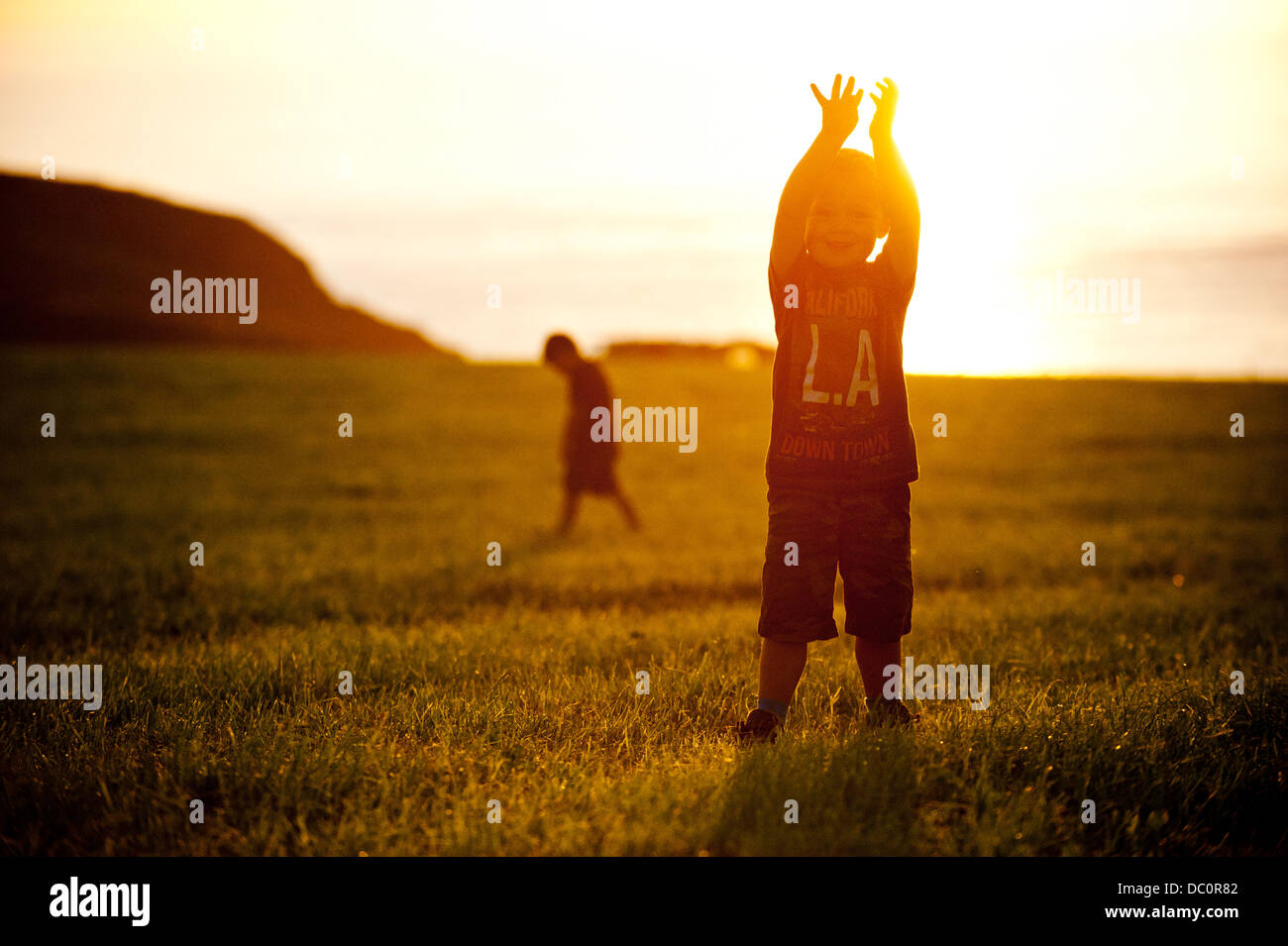 Children jumping and playing in front of a setting sun near St Davids, Pembrokeshire, Stock Photo