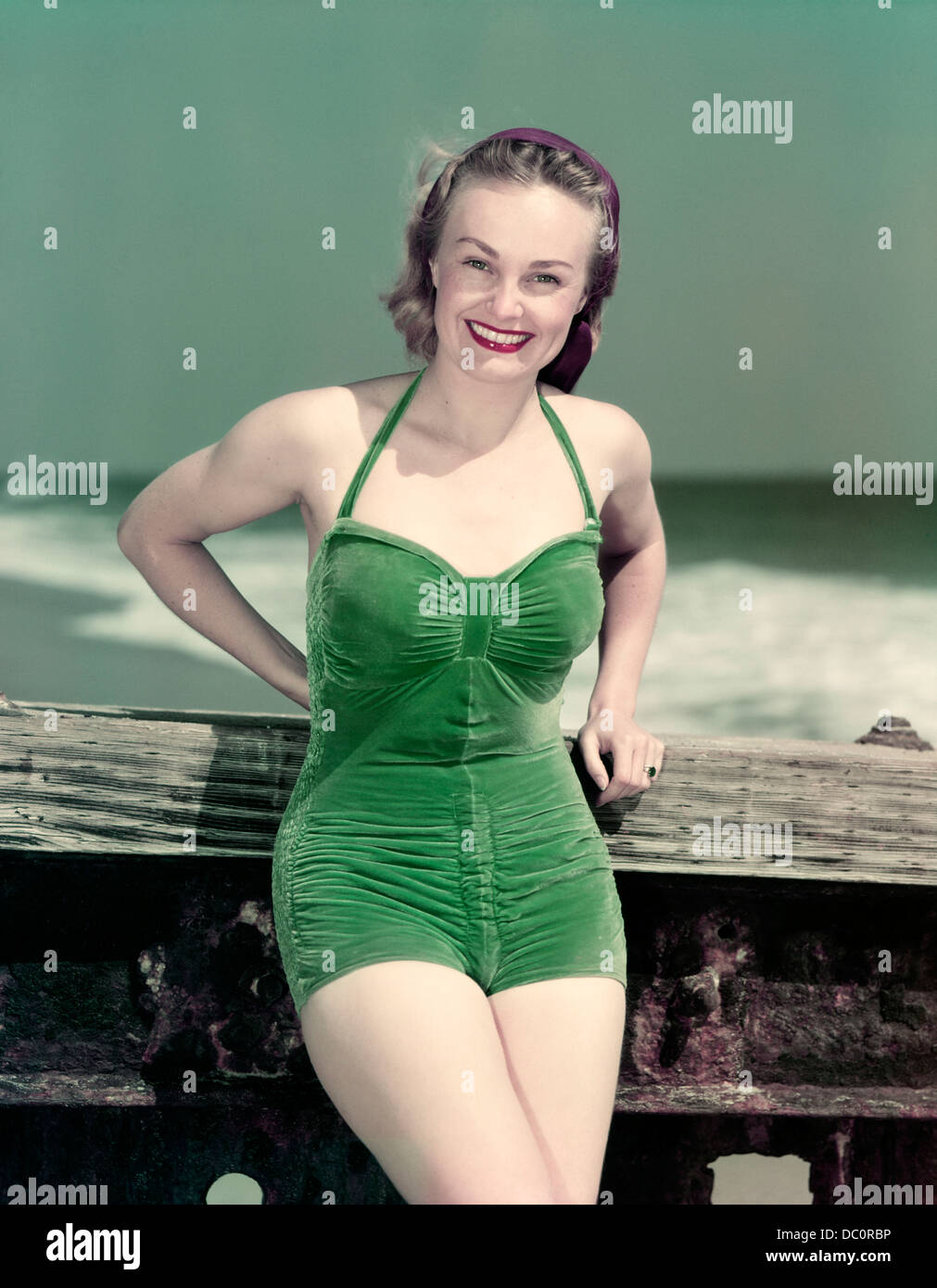 1940s PORTRAIT SMILING WOMAN WEARING GREEN VELVET BATHING SUIT POSING LEANING ON DIVING BOARD Stock Photo