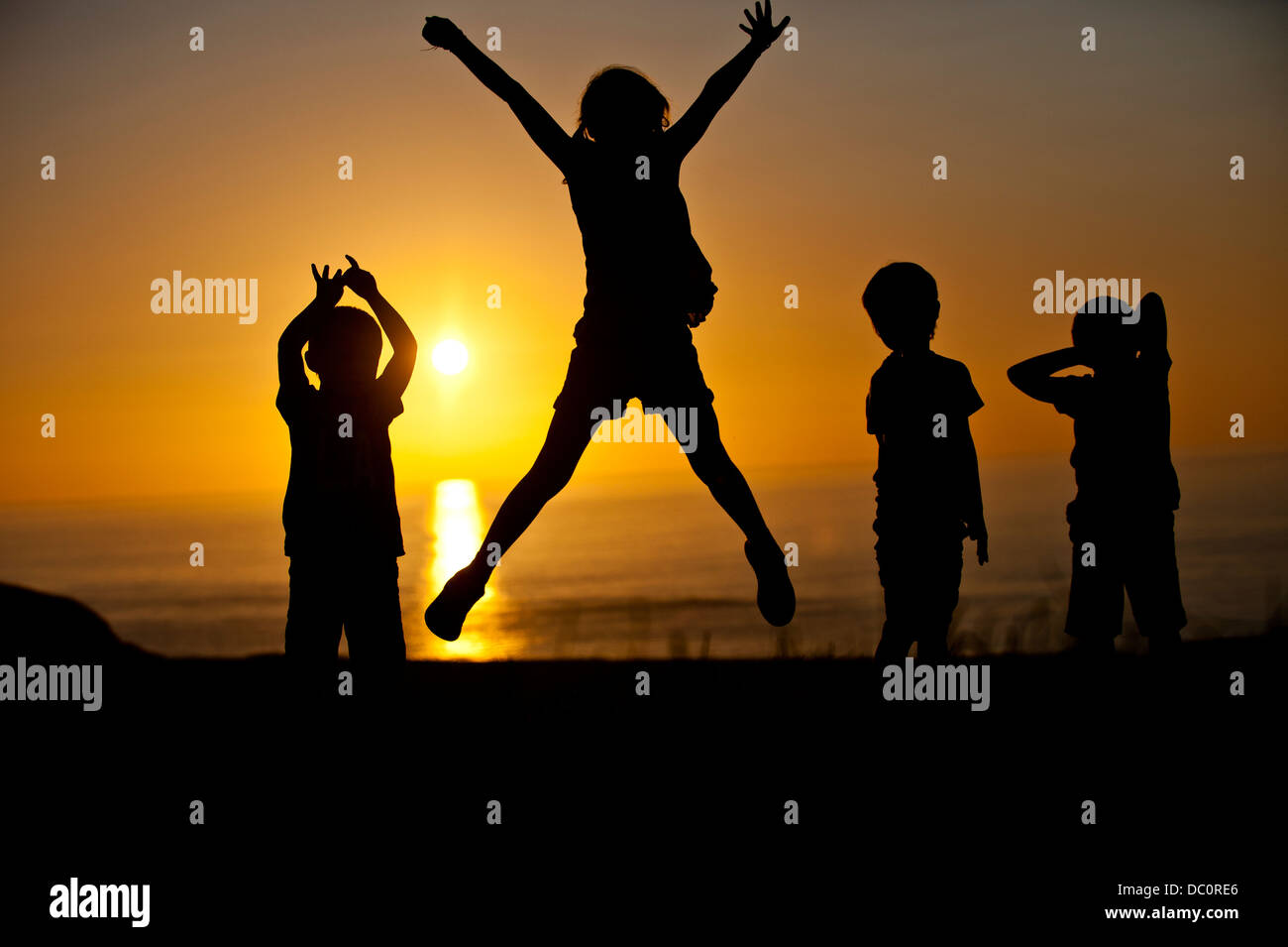 Children jumping and playing in front of a setting sun near St Davids, Pembrokeshire, Stock Photo