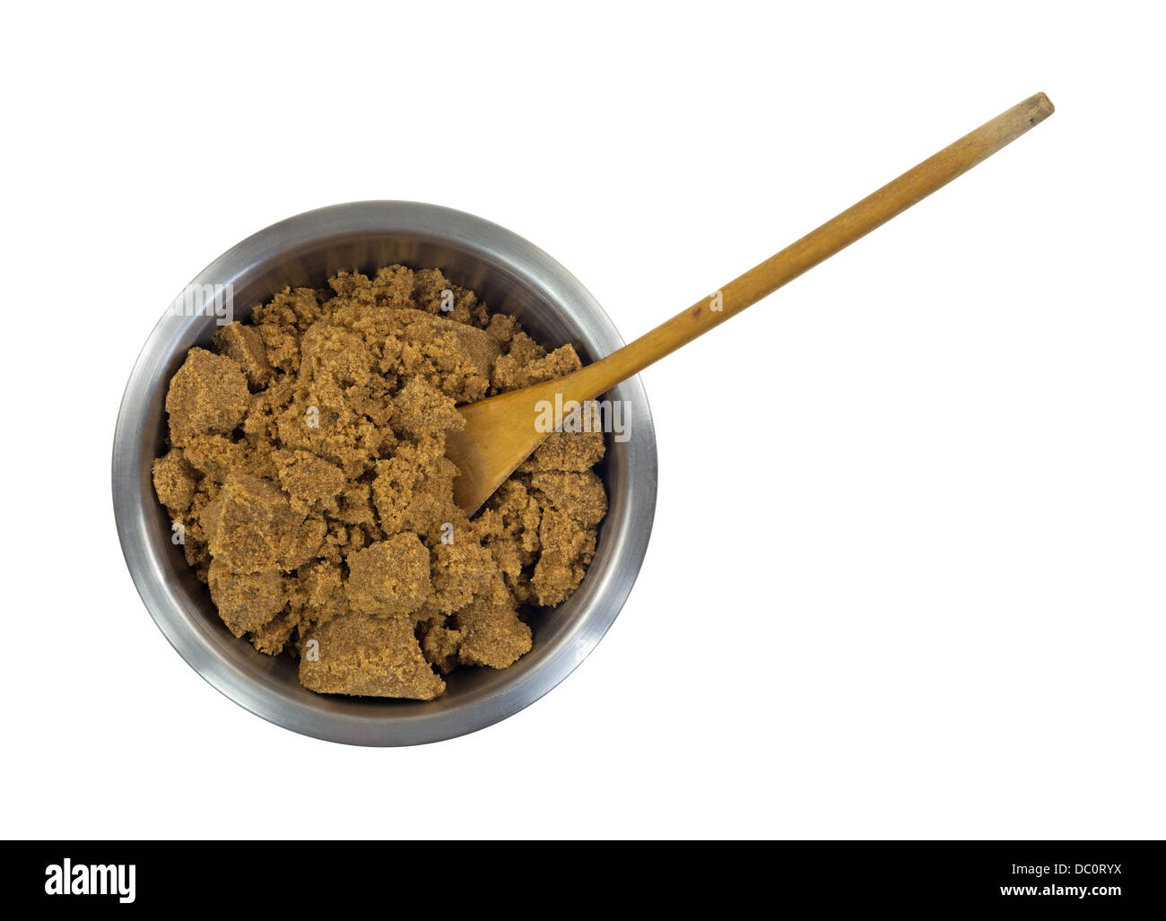A stainless steel bowl filled with dark brown sugar and a worn wood spoon on a white background. Stock Photo