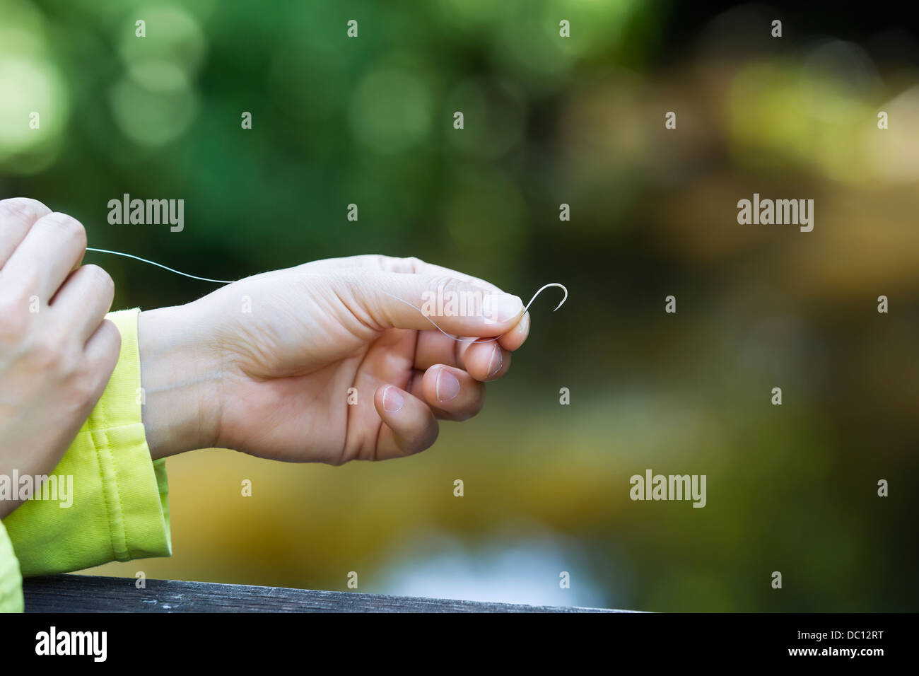 Horizontal photo of female hand pinching small fishing hook with blurred  out trees in background Stock Photo - Alamy