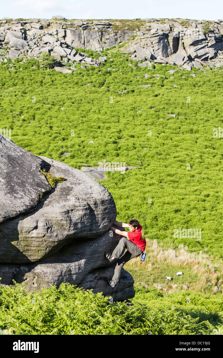 a man in a red t-shirt climbing and bouldering at Burbage Valley in the Peak District National Park near Sheffield, England UK Stock Photo