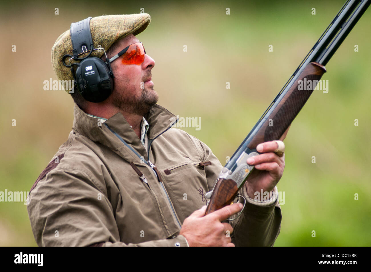 Man shooting at a simulated game shooting clay shoot wearing tweed cap, ear and eye protection Stock Photo