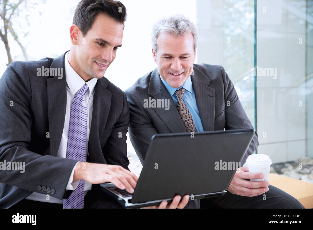 Businessmen drinking coffee and sharing laptop Stock Photo
