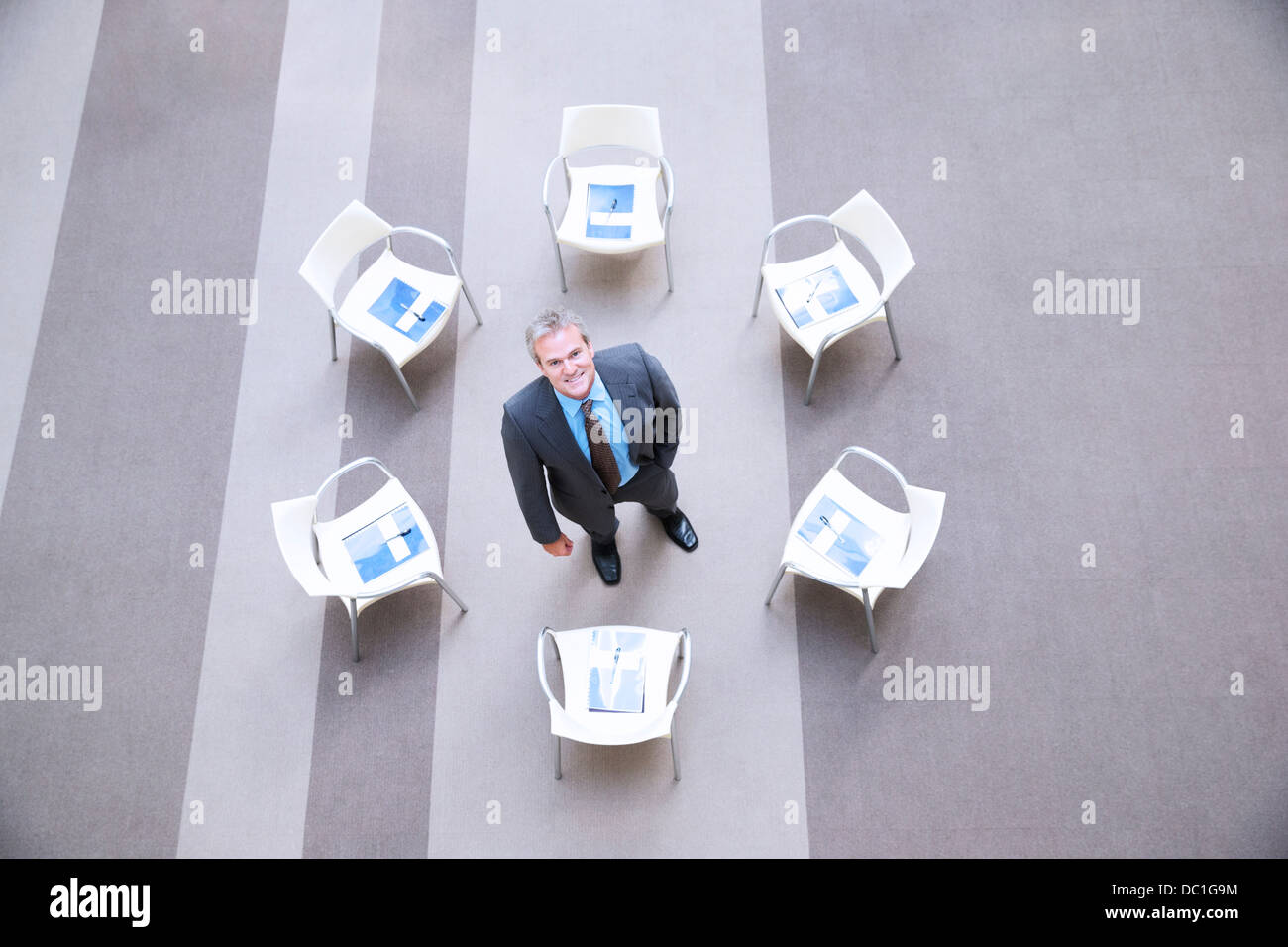 High angle portrait of smiling businessman at center of chairs in circle Stock Photo
