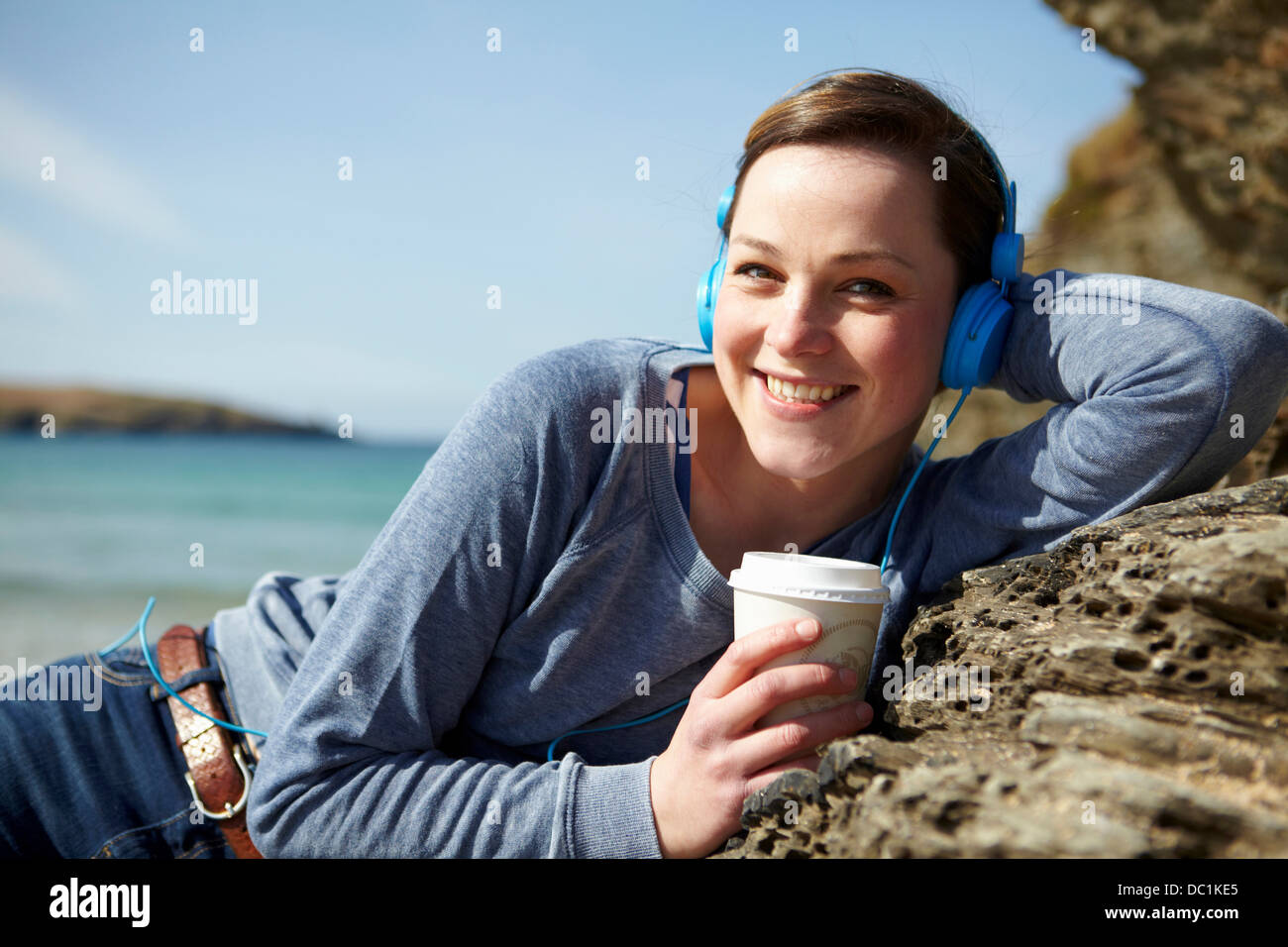Portrait of young woman at coast with coffee and earphones Stock Photo